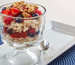 A tall glass of creamy rice layered with berries and topped with granola