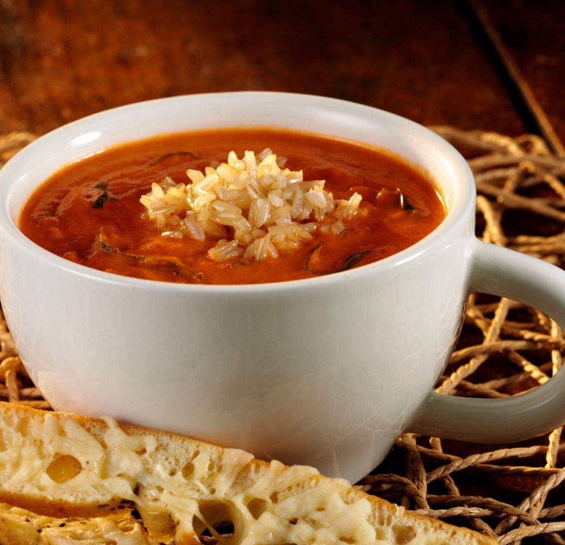 One mug full of creamy tomato soup mixed with basil, a dollop of rice in the middle and crunchy bread