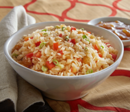 A small bowl of rice mixed with chopped peppers, coconut, raisins and mango chutney to the side