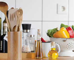 A kitchen countertop covered with vegetables, cooking oils and cooking utensils
