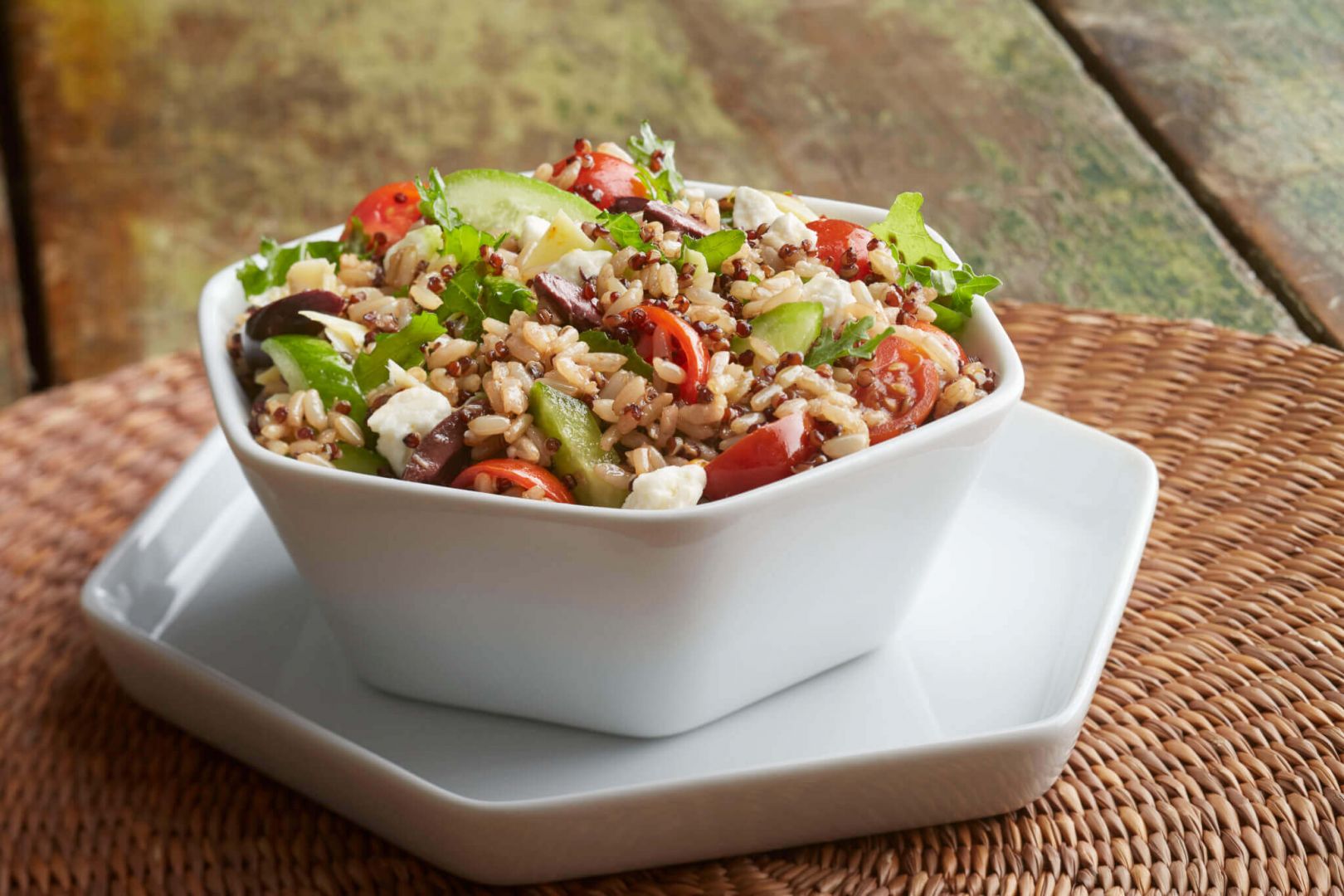 A small salad bowl filled with quinoa, chopped lettuce, cucumber, tomatoes, olives and feta cheese